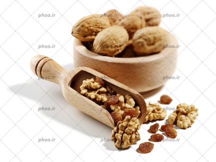 عکس با کیفیت گردو ها داخل ظرف چوبی و مغز گردو داخل پیمانه چوبی و چند کشمش در کنارش