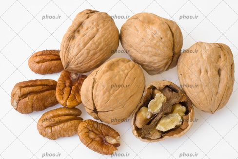 عکس با کیفیت چند گردو تازه با پوست در کنار چند مغز گردو در بک گراند سفید