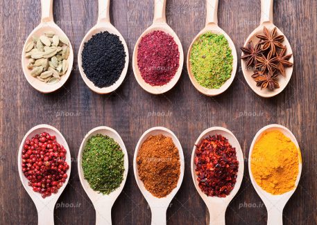 عکس با کیفیت گیاهان دارویی سیاه دانه و ادویه جات زرد چوبه و هل و سماق در قاشق های چوبی بزرگ قرار گرقته در کنار هم به صورت موازی