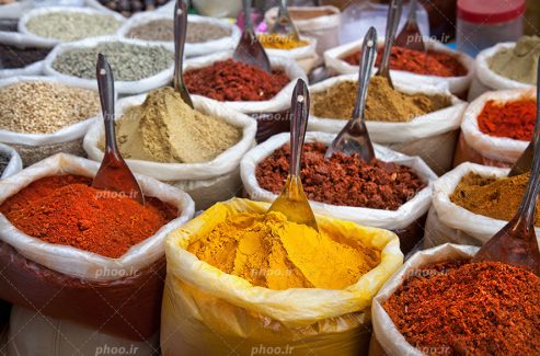 عکس با کیفیت زرد چوبه و دارچین و فلفل قرمز و پودر زنجبیل و چند دارو گیاهی دیگر داخل پلاستیک های بزرگ چیده شده در کنار یکدیگر