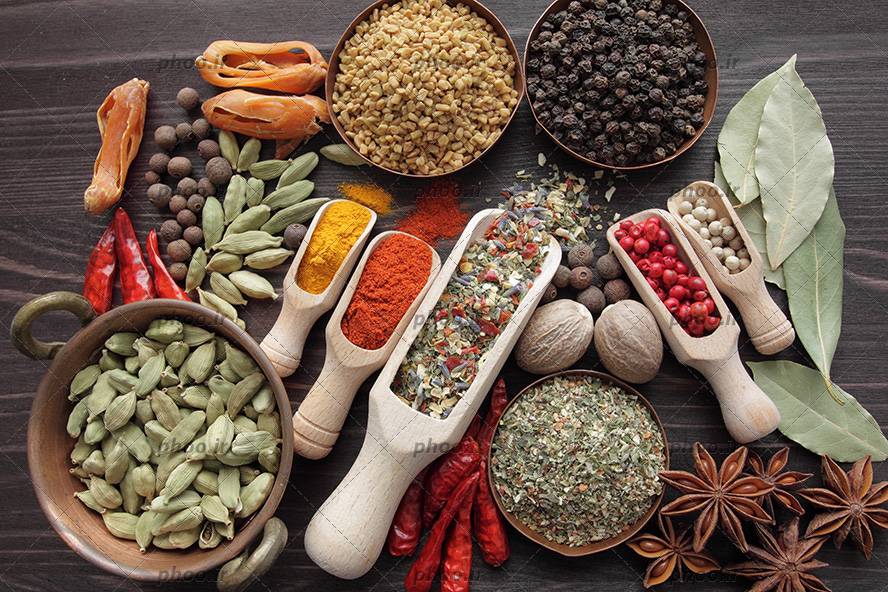 عکس با کیفیت پیمانه های چوبی پر شده از گیاهان دارویی و ادویه جات مثل زرد چوبه و فلفل قرمز و همچنین برگ بو و ظرف هل و چند ظرف دارو گیاهی در کنارش