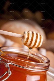 عکس با کیفیت برداشتن عسل از شیشه عسل با قاشق چوبی عسل از نمای نزدیک