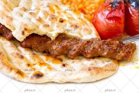 عکس با کیفیت کباب کوبیده بر روی نان و دوعدد گوجه در کنارش