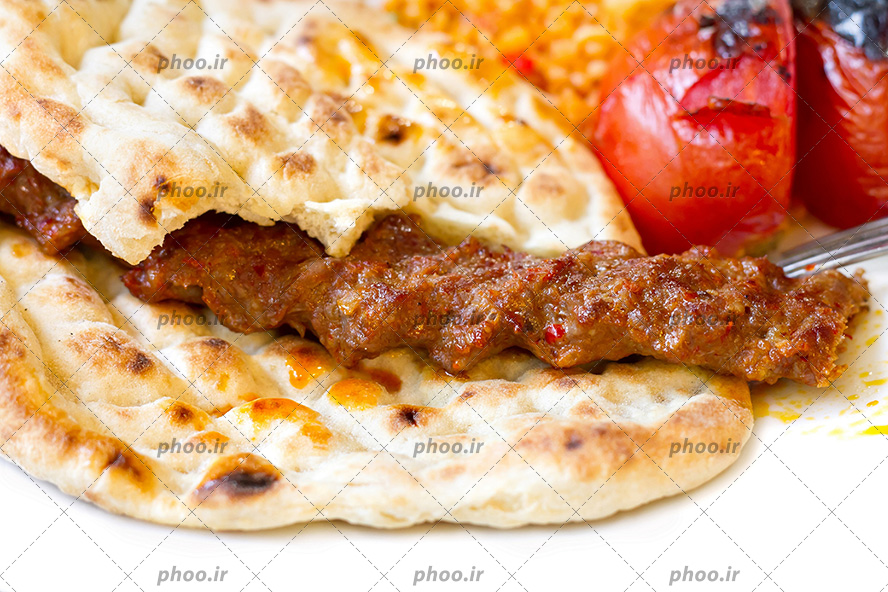 عکس با کیفیت کباب کوبیده بر روی نان و دوعدد گوجه در کنارش