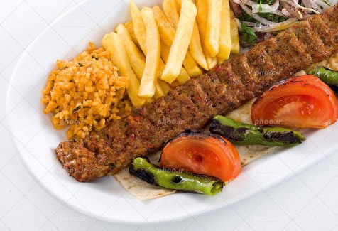 عکس با کیفیت کباب کوبیده در کنار سیب زمینی سرخ شده و گوجه و فلفل سبز و پیاز در دیس سفید