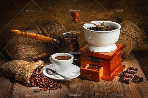 عکس با کیفیت فنجان سفید قهوه و گونی کنفی و قهوه جوش دستی و آسیاب دستی قهوه در کنار یکدیگر