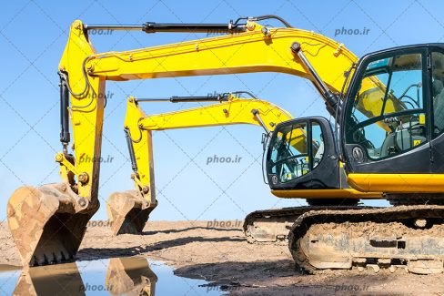 عکس با کیفیت بیل مکانیکی با بدنه ی زرد رنگ در حال کندن و گود برداری زمین و مقدار آبی جمع شده بر روی زمین