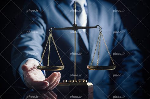 عکس با کیفیت ترازو عدالت مقابل دست مرد با کت شلوار با بکگراند مشکی