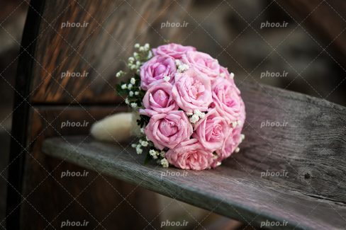 عکس با کیفیت دسته گل عروس با گل های صورتی بر روی نیمکت چوبی