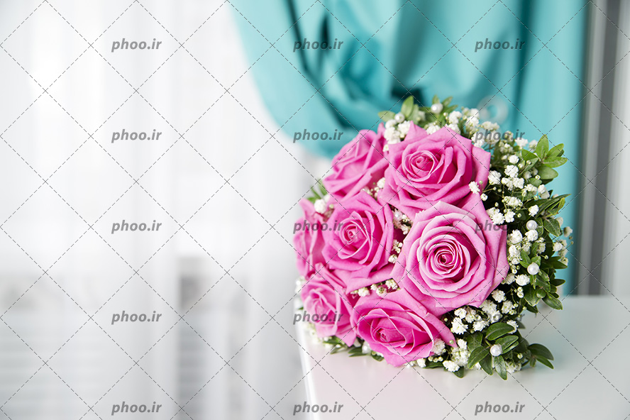 عکس با کیفیت دسته گل عروس با گل های رز صورتی و تزئینات زیبا و قرار گرفته بر روی میز