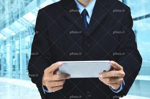 عکس با کیفیت مرد با کت و شلوار شیک ایستاده در اداره و در حال کار کردن با گوشی