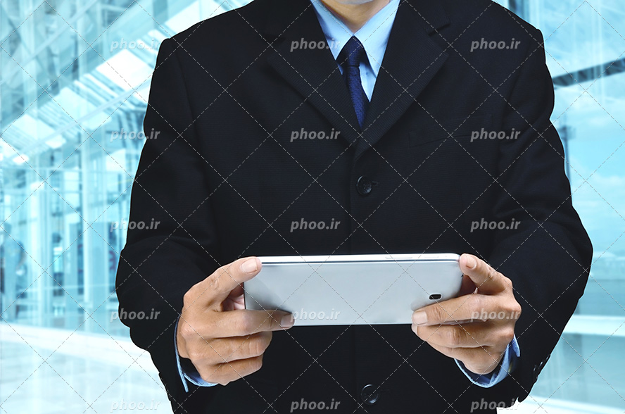 عکس با کیفیت مرد با کت و شلوار شیک ایستاده در اداره و در حال کار کردن با گوشی