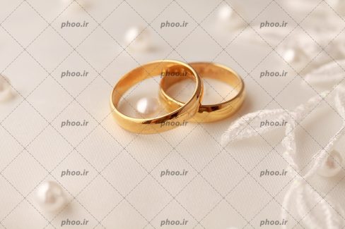 عکس با کیفیت دو حلقه ازدواج به رنگ طلایی بر روی پارچه سفید لباس عروس