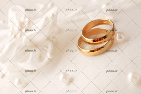 عکس با کیفیت دو حلقه ی طلایی در کنار گل های پارچه ای و مروارید های دوخته شده بر روی پارچه