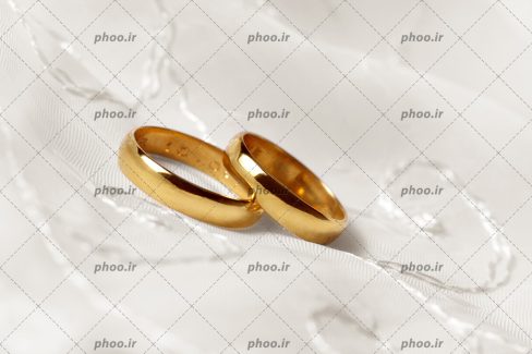 عکس با کیفیت دو رینگ طلایی مناسب برای حلقه ی ازدواج بر روی پارچه ی سفید گلدوزی شده