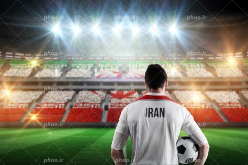 عکس با کیفیت فوتبالیست تیم ملی با لباس سفید در ورزشگاه و صندلی های ورزشگاه رنگ شده به شکل پرچم ایران