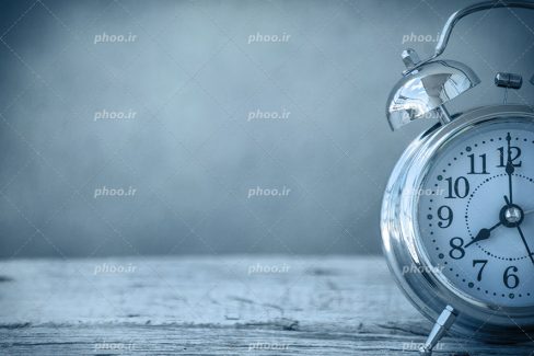 عکس با کیفیت ساعت زنگدار به رنگ نقره ای قرار گرفته بر روی میز چوبی