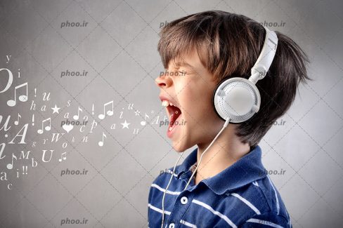 عکس با کیفیت هدفون بر روی گوش کودک و کودک در حال خواندن آهنگ با صدای بلند و بیرون آمدن نت ها از داخل دهانش
