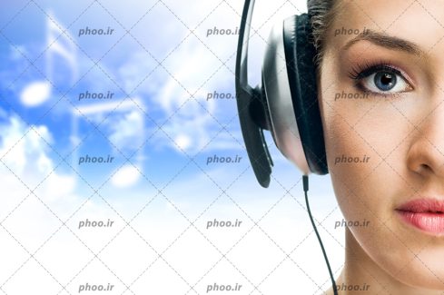 عکس با کیفیت زن در حال گوش دادن به گوشی به کمک هدفون و پس زمینه آسمان آبی و ابر های شبیه به نت موسیقی