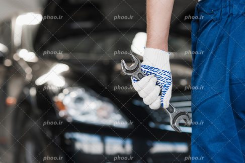 عکس با کیفیت تعمیرکار آچار به دست با لباس مخصوص در حال تعمیر ماشین مشکی لوکس