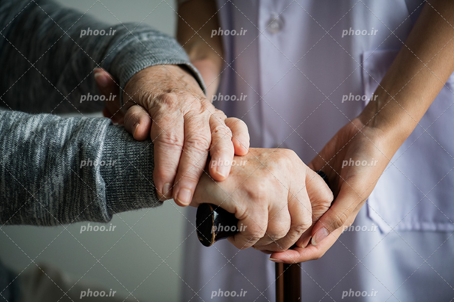 عکس با کیفیت پیرزن عصا به دست و پرستار خوش قلب در حال کمک کردن به پیرزن