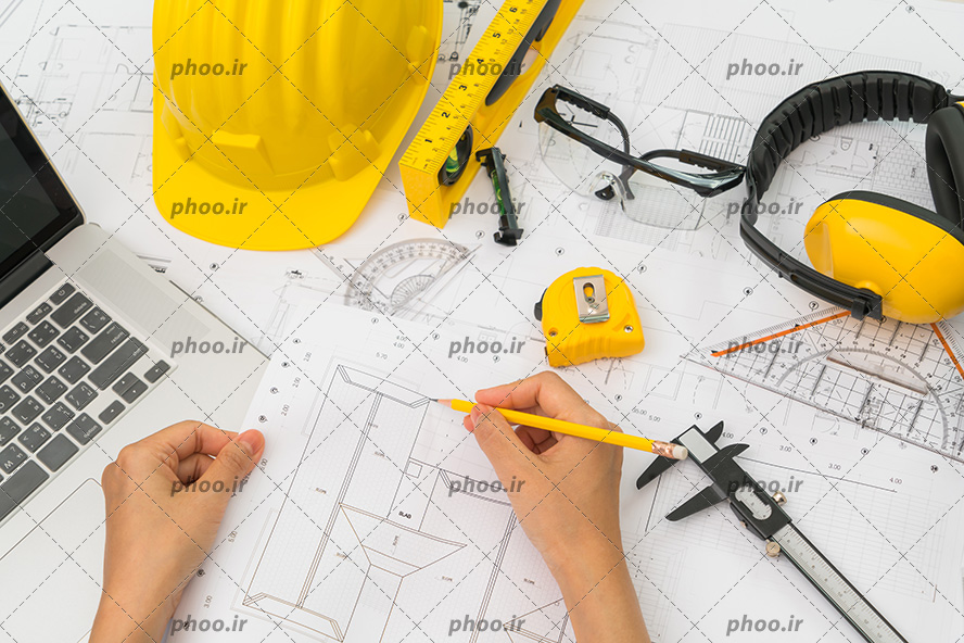 عکس با کیفیت لوازم معماری و لپ تاپ در کنار مهندس عمران در حال نقشه کشی
