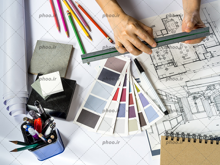 عکس با کیفیت مهندس نقشه کش در حال کشیدن نقشه و مقوا های کنتراست رنگ و جامدادی و در کنار دست او