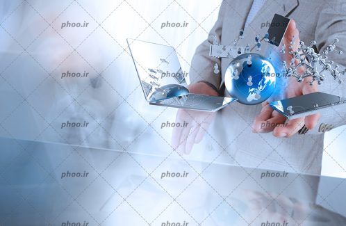 عکس با کیفیت مرد ایستاده با کت و شلوار خاکستری و لپ تاپ و گوشی همراه و کره زمین معلق در هوا