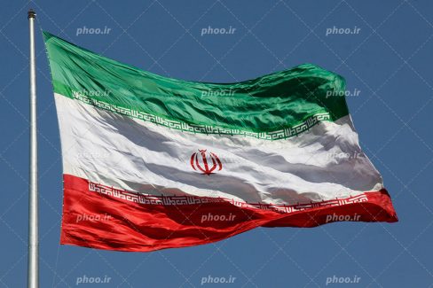عکس با کیفیت پرچم زیبا و باشکوه ایران در آسمان در حال تکان خوردن به دلیل وزش باد