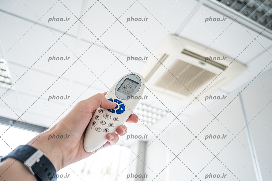 عکس با کیفیت مرد در حال استفاده از ریموت کولر گازی و کم کردن درجه ی آن