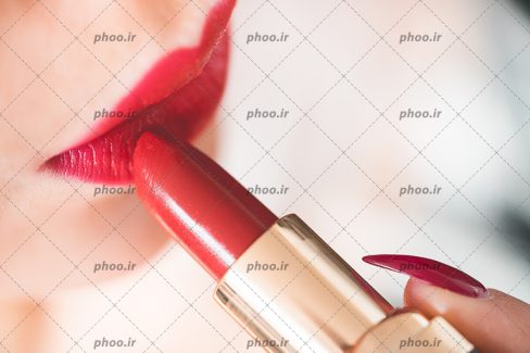 عکس با کیفیت زن در حال استفاده از رژ قرمز بر روی لب هایش از نمای نزدیک
