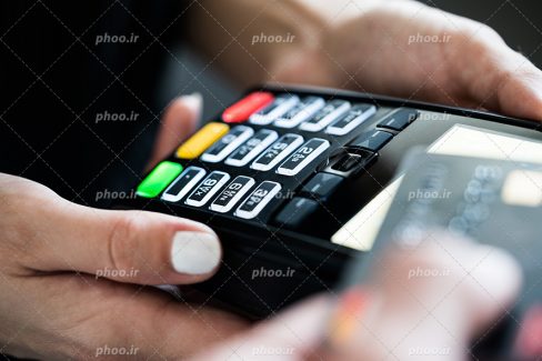 عکس با کیفیت دستگاه پوز مشکی در دستان زن فروشنده و در حال حساب کردن اجناس مشتری