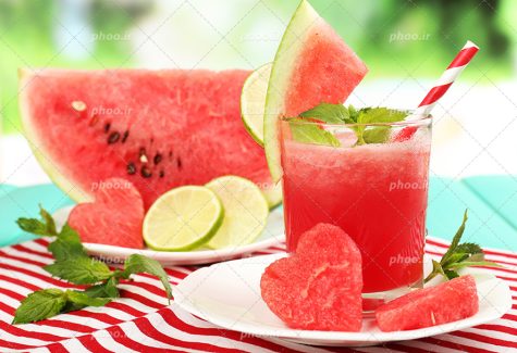 عکس با کیفیت اسلایس نیمه ی هندوانه و برش هایی از لیمو تازه در کنار آب طبیعی هندوانه بر روی پارچه ای راه راه قرمز و سفید