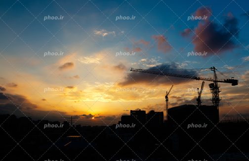 عکس با کیفیت ساختمان کوتاه و بلند نیمه ساز در کنار تاور کرین با کنتراست بالای تصویر و آسمان زیبا در حال غروب