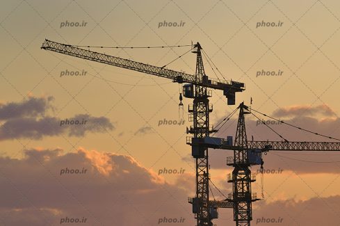 عکس با کیفیت دو تاور کرین کوچک و بزرگ از زاویه پایین در آسمان در حال غروب