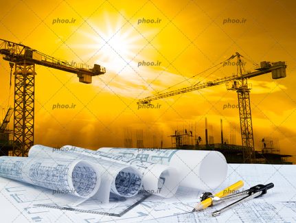 عکس با کیفیت نقشه های ساختمانی در کنار پرگار و خط کش و در پشت آنها تاور کرین ها و ساختمان های نیمه ساز و نور نارنجی خورشید