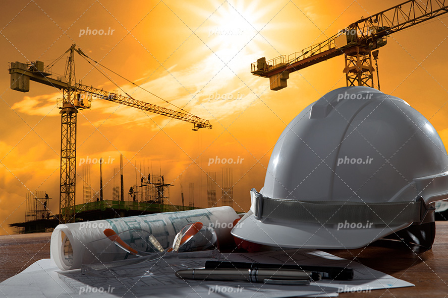 عکس با کیفیت کلاه ایمنی سفید و عینک مهندسی و دو روان نویس بر روی نقشه های ساختمانی و تاور کرین ها و ساختمان های نیمه ساز