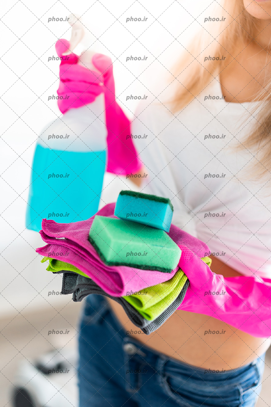 عکس با کیفیت چند دستمال و دو اسفنج در دستان زن با دستکش های ظرف شویی صورتی و محلول پاک کننده در دست دیگر