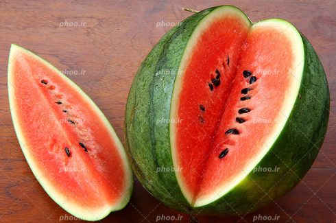 عکس با کیفیت هندوانه ی قاچ شده ی قرمز و تازه قرار گرفته بر روی میز چوبی