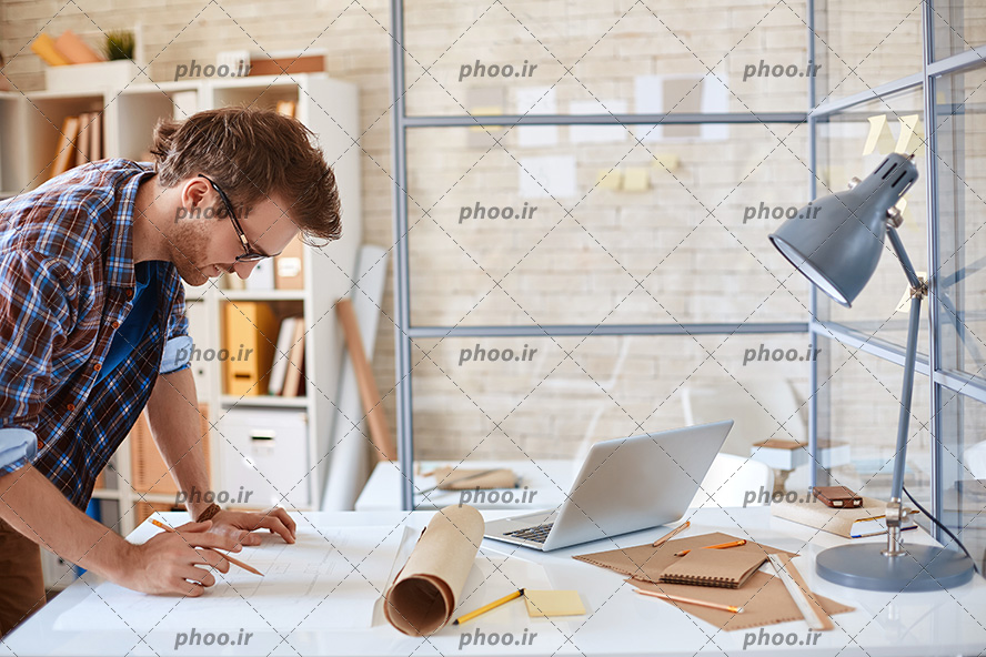 عکس با کیفیت اتاق کار و مهندس در حال برسی و کشیدن نقشه ساختمان