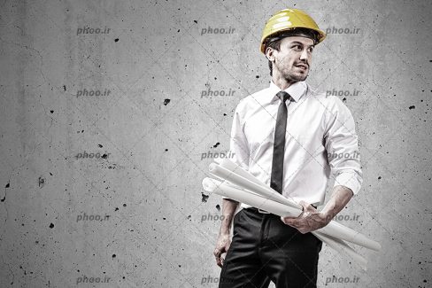 عکس با کیفیت مرد ایستاده و نقشه به دست و کلاه ایمنی بر سر او و پس زمینه طوسی
