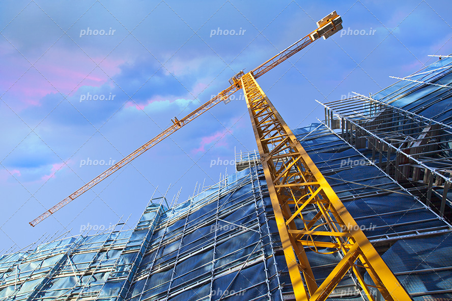 عکس با کیفیت تصویر از زاویه پایین یک تاور کرین در کنار ساختمان مرتفع و آسمان زیبا