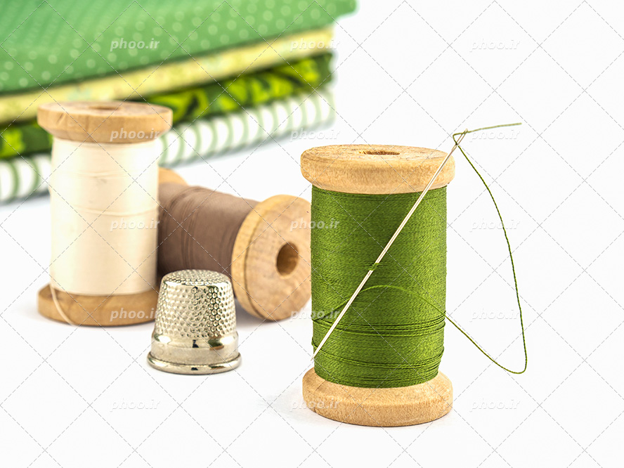 عکس با کیفیت پارچه های سبز خال خالی و راه راه و ساده در کنار نخ های سبز و قهوه ای و کرم در پس زمینه سفید