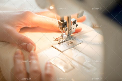 عکس با کیفیت چرخ خیاطی و دستان زن بر روی آن و نور روشن چرخ خیاطی افتاده بر دستان زن