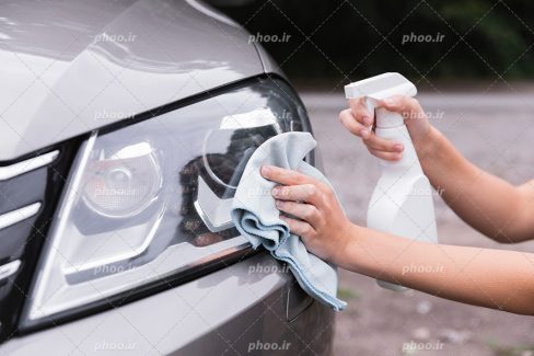عکس با کیفیت تمیز کردن شیشه چراغ جلو ماشین توسط مرد با شیشه پاک کن و دستمال