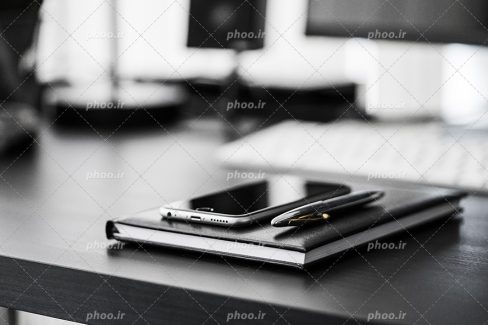 عکس با کیفیت موبایل و خودکار قرار گرفته بر روی دفتر در داخل شرکت