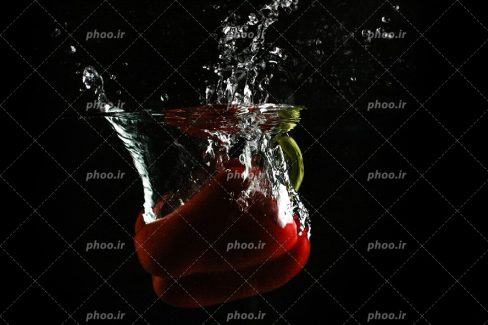 عکس با کیفیت منحصفرد فلفل دلمه ای قرمز در حال غرق شدن در آب و پس زمینه به رنگ مشکی