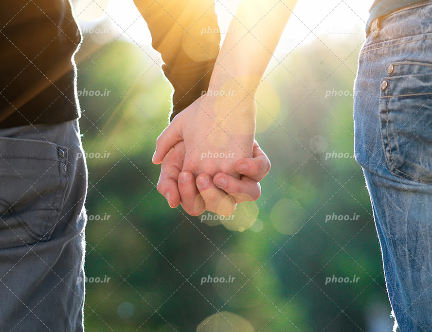 عکس با کیفیت بسیار زیبا زن و مرد دست در دست یکدیگر ایستاده در طبیعت و تابش نور خورشید