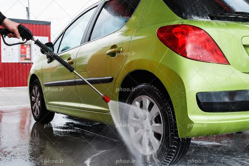 عکس با کیفیت بسیار زیبا مرد در حال شستن لاستیک های ماشین سبز به کمک شیلنگ مخصوص کارواش