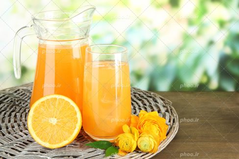 عکس با کیفیت پارچ و لیوان حاوی آب پرتقال بر روی سبد حصیر و پرتقال در کنار آنها